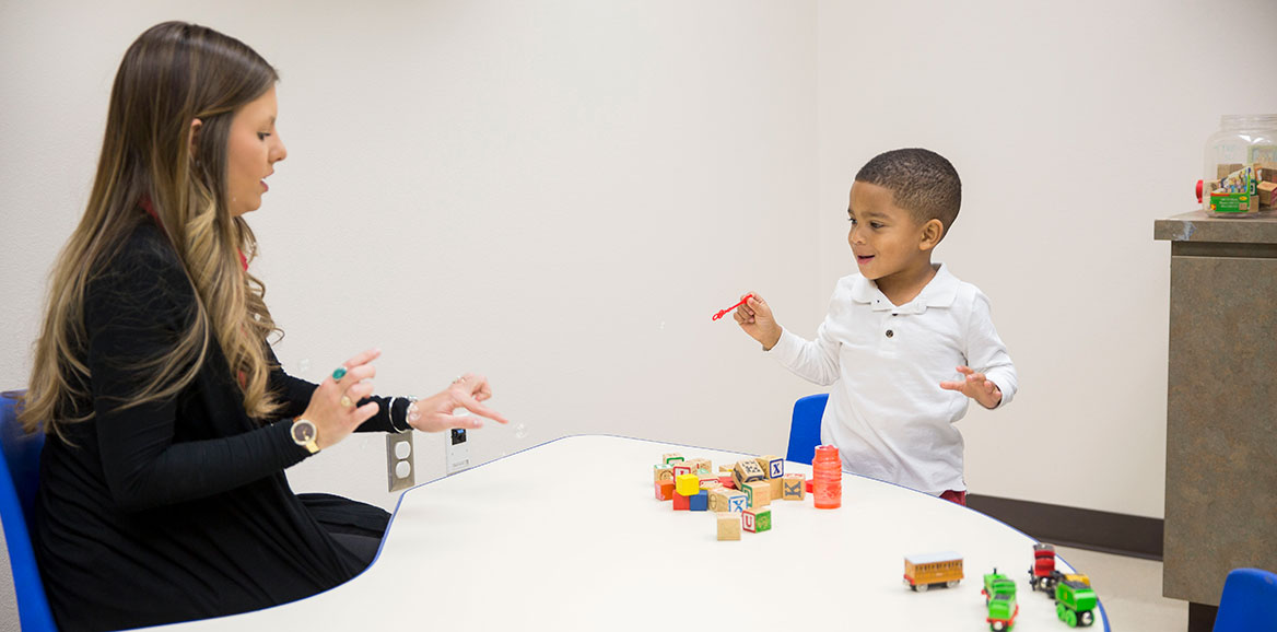 Speech student uses bubbles and blocks to interact with a child during a session