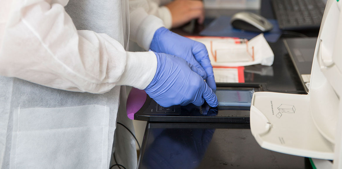 A student's gloved hands placing a slide onto the tray of a machine in the lab